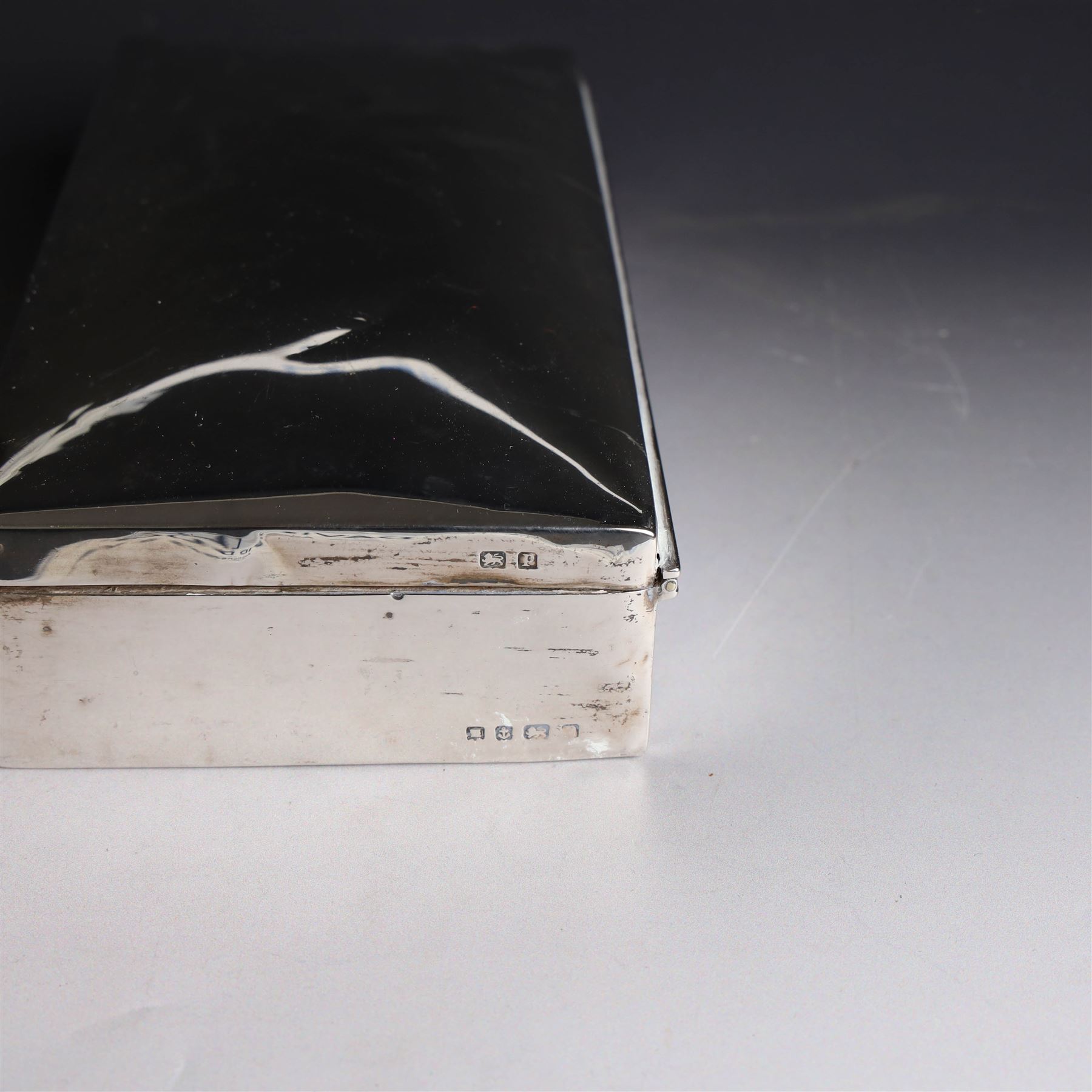 Two silver cigarette boxes, comprising early 20th century plain rectangular example with compartmentalised softwood interior, hallmarked Birmingham 1914, maker's mark indistinct, and an early 20th century example with engine turned decoration and engraved initials to cover, hallmarks worn and indistinct, largest H4.5cm, W21cm