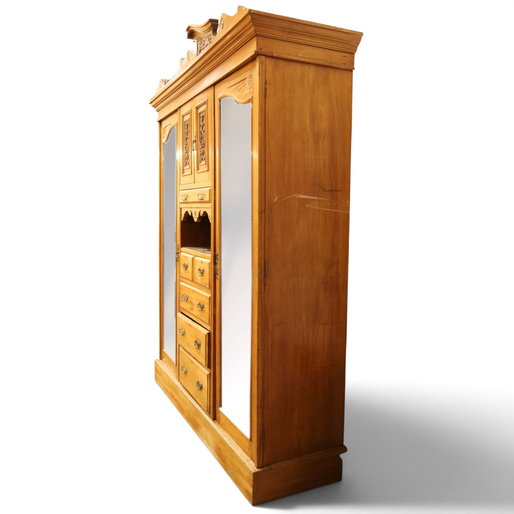 Edwardian walnut triple combination wardrobe, projecting pediment with pierced foliate scroll cresting above a central cupboard flanked by bevelled mirrored doors, over open recess with mirrored back, above two short and three long drawers with brass handles, interior fitted with hanging rails and shelf, raised on plinth base