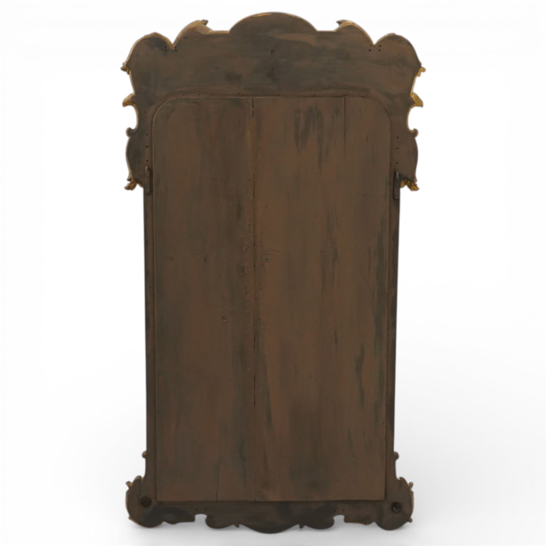 In the manner of Thomas Johnson - circa 1900 Georgian Revival giltwood wall mirror, the shaped rectangular plate within a foliate and scallop carved slip and richly ornamented frame, surmounted by a pierced cartouche crest centred with a protruding relief carved winged cherub mask and issuing scrolling acanthus and floral ornament, the sides with eagle masks over acanthus scrolls, terminating in a shaped apron with moulded rosette and spiralling acanthus leaves