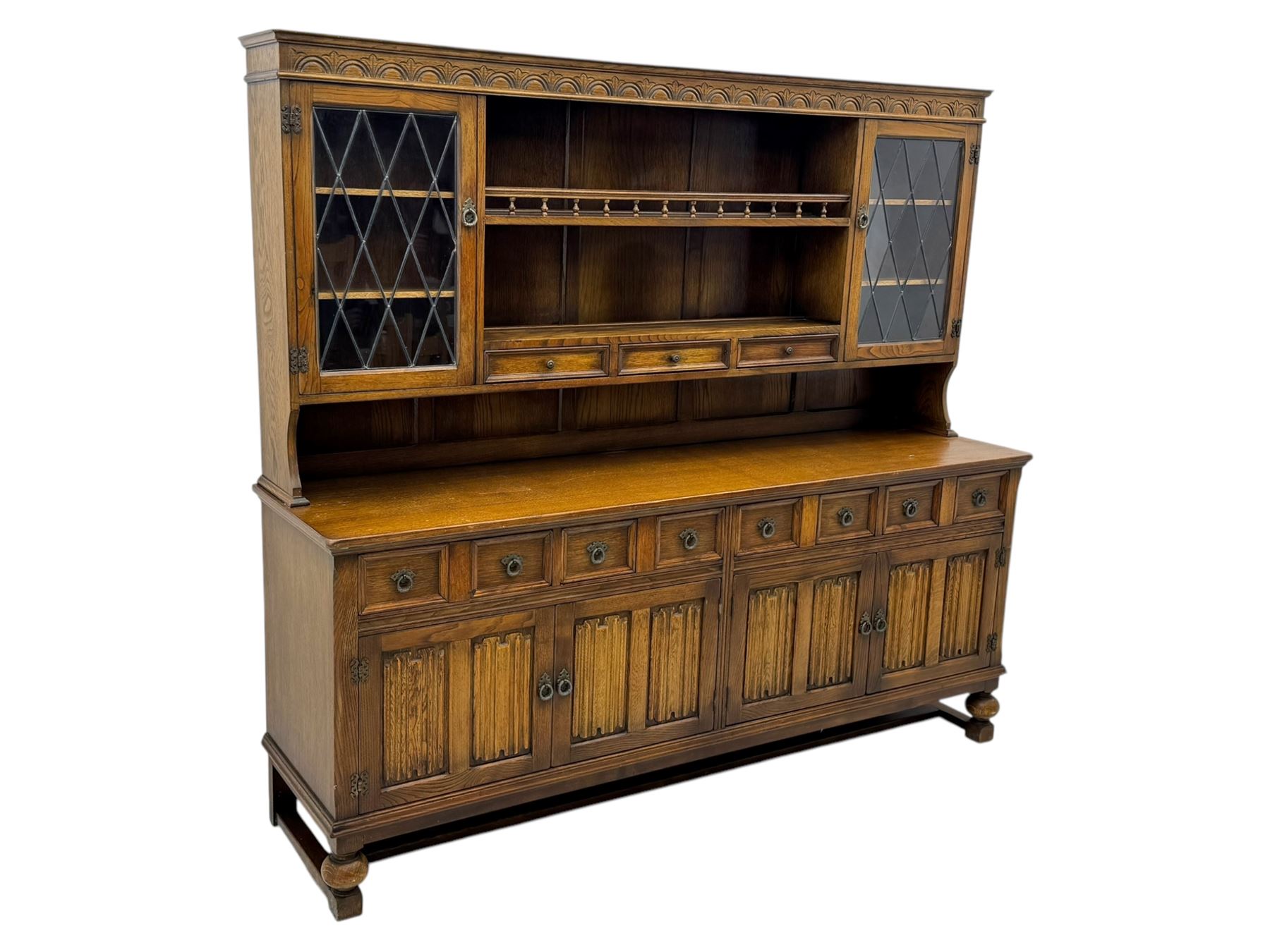 Large mid-20th-century oak dresser with two astragal glazed doors between gallery shelf and lower shelf, with three short drawers and lower section with four drawers and three double-panelled linen-fold hinged cupboard doors 