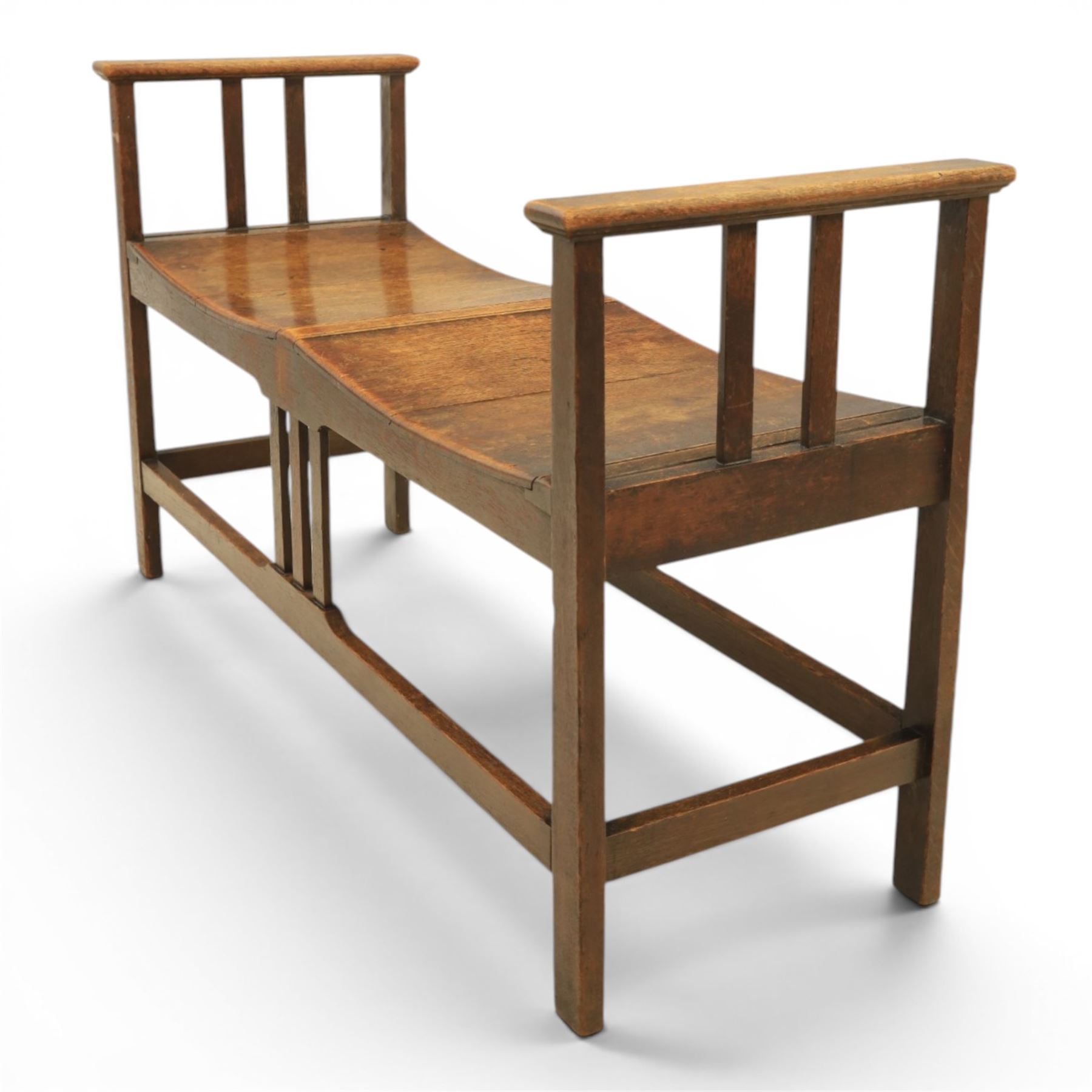 Arts and Crafts oak window bench, with flat armrests flanking two dished seats, raised on square supports united by stretchers
