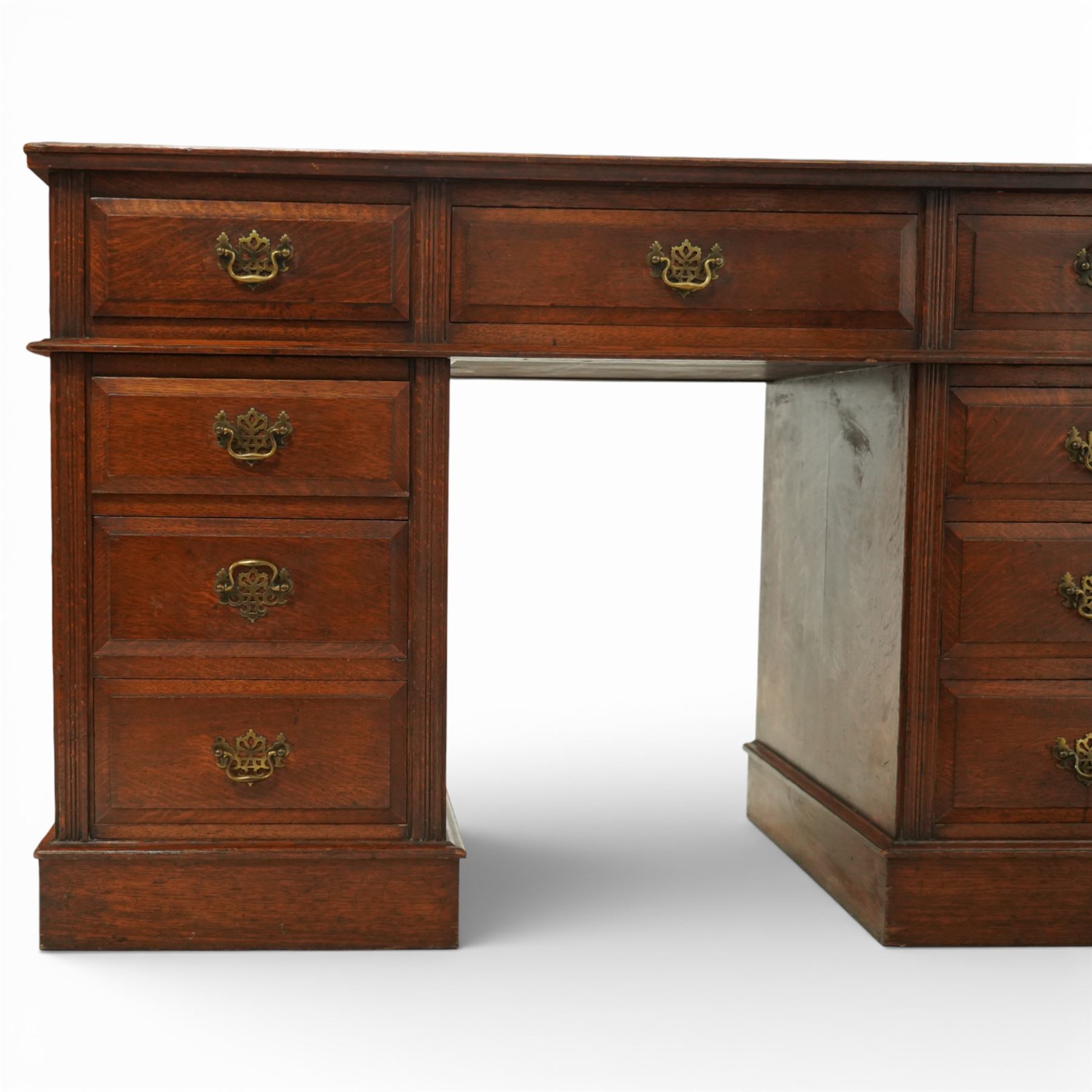 Late Victorian oak nine drawer desk, the rectangular top inset with a tooled leather writing surface bordered in gilt, above three frieze drawers and two pedestal cupboards each fitted with three graduated drawers, all with brass swan neck handles, raised on plinth bases