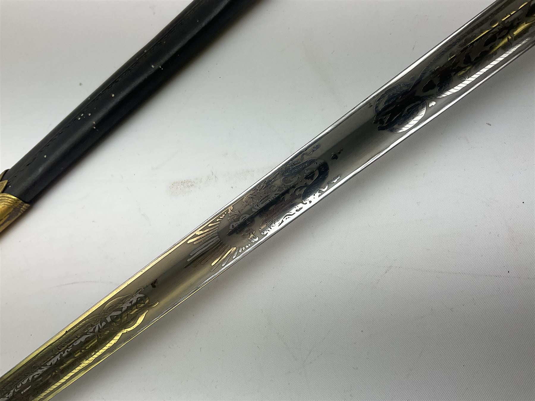 WW1 George V era 1827 Pattern Royal Naval Officer’s sword, the 80cm fullered steel blade decorated with crown, fouled anchor etc and marked Gieves Portsmouth London Edinburgh Devonport to the ricasso, gilded hilt with fouled anchor and crown, wire-bound ray skin grip, lion’s head pommel with mane backstrap, folding/locking langet and full bullion knot; in  leather scabbard having twin brass lockets with hand engraved panels and twin suspension rings L94cm overall. Provenance: By direct family descent from Brian Heathcote HMS Conqueror later Superintendant in the Liverpool Special Constabulary.