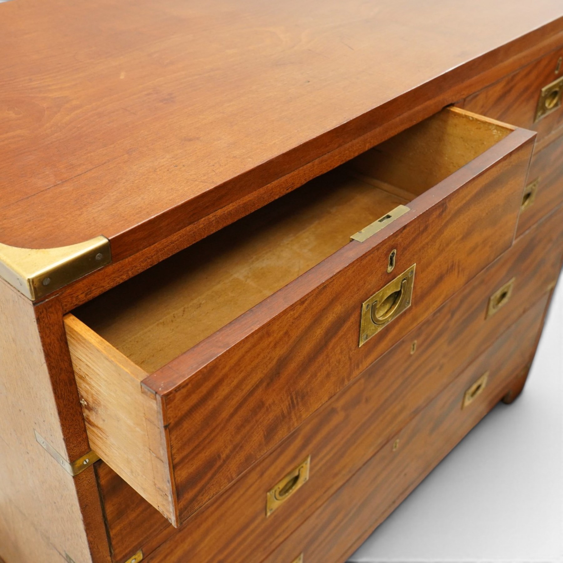 19th century figured mahogany military campaign chest of drawers in two sections, the rectangular top with brass-bound corners over two short and three long graduated drawers, each fitted with recessed brass campaign handles and escutcheons, the carcass with brass strapwork and carrying handles to the sides, raised on short bracket feet