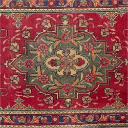 North West Persian Tabriz hand-knotted runner, madder red field with central octagonal medallions of sage green, navy and ivory, ground enclosing a floral rosette and radiating angular vinery, scrolling floral sprays and palmettes either end with shaped pendants principal border on navy ground decorated with a continuous vine-scroll of palmettes and rosettes, flanked by narrow guard borders, with cotton fringe ends 