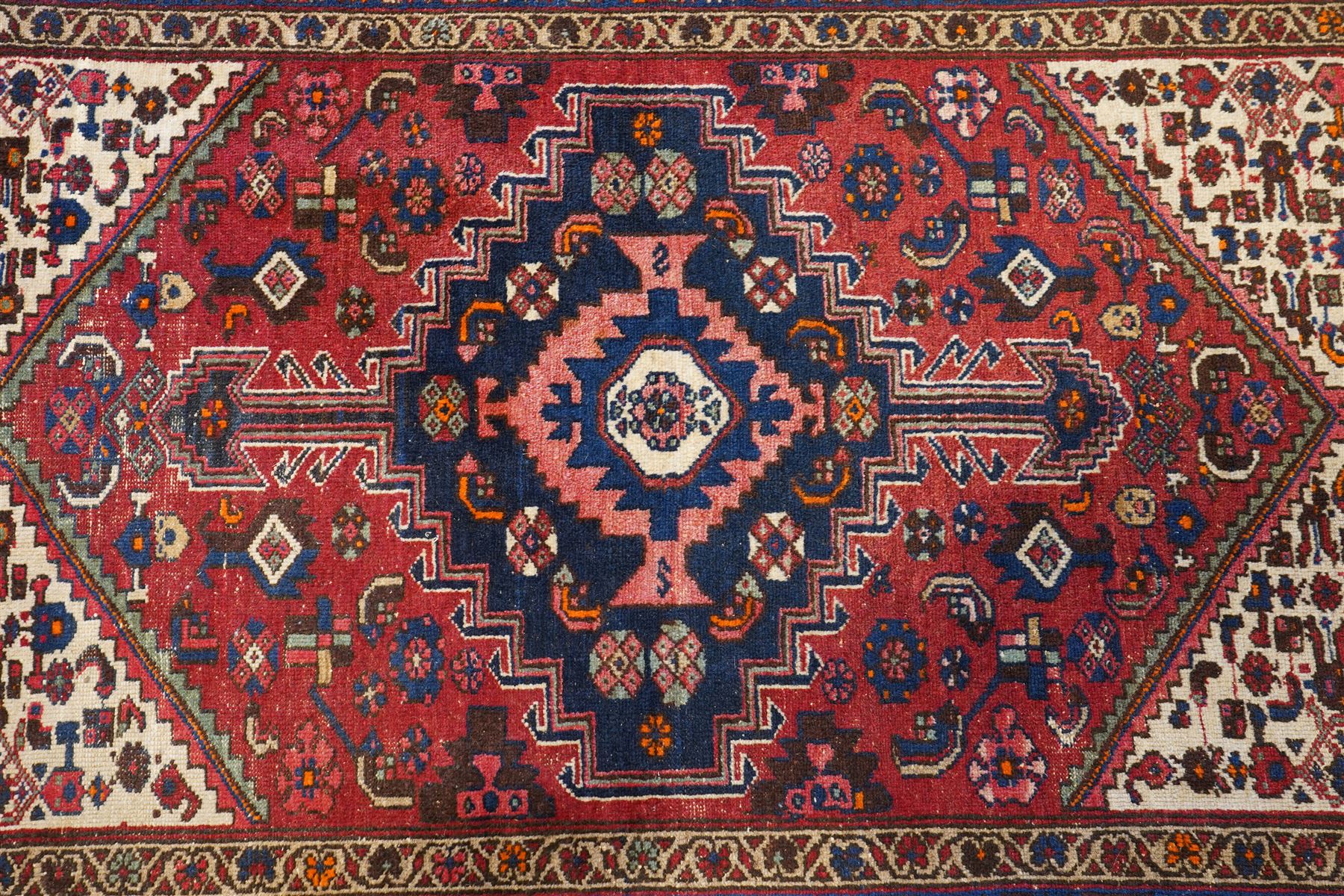 Persian Heriz crimson ground carpet, the central navy geometric medallion on a red crimson ground field, surrounded by further geometric stylised motifs and foliate designs, enclosed by multiple guard-lines  
