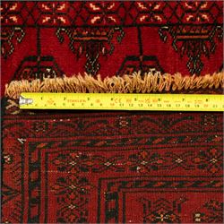 Turkman hand-knotted carpet, deep red ground, with an all-over field of repeating gul motifs arranged in rows, enclosed by multiple red geometric borders with stylised flowerheads and hooked motifs, flanked by narrow patterned guard stripes, with wool fringes