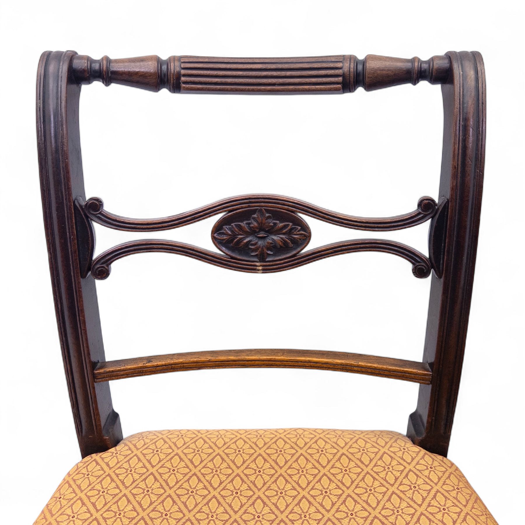Pair of Regency mahogany side chairs, reeded bar backs centred by oval paterae, overstuffed seats upholstered in gold geometric patterned fabric, on turned tapering front supports 