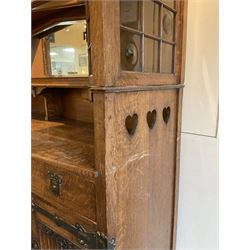 Shapland and Petter - Arts & Crafts period oak dresser, raised gallery top with spade balustrade, central bevelled mirror flanked by two cabinet, astragal glazed doors with yellow tinted glass and bullseye panes, the sides with pierced heart shaped decoration, fitted with two drawers and two double cupboards, enclosed by linenfold panelled doors,  copper work strap hinges and fixtures, on shaped spade feet, the locks stamped 'S&P'