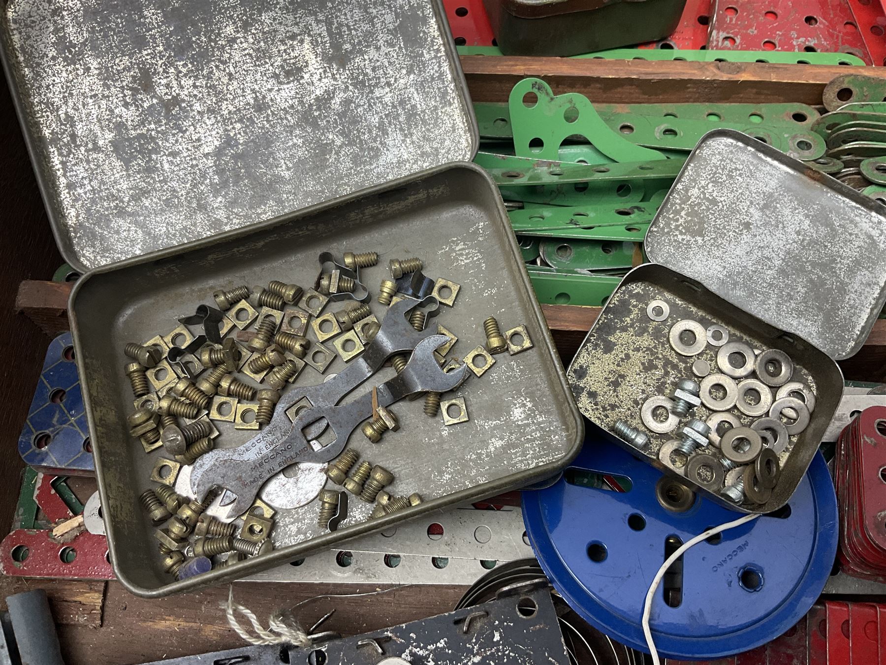 Meccano - large quantity of loose parts including various plates and strips, flanged plates, pulleys, axle rods and crank handles, wheels and tyres, gear wheels, brackets, nuts & bolts, various manuals; predominantly red and green; some in compartmentalised wooden trays