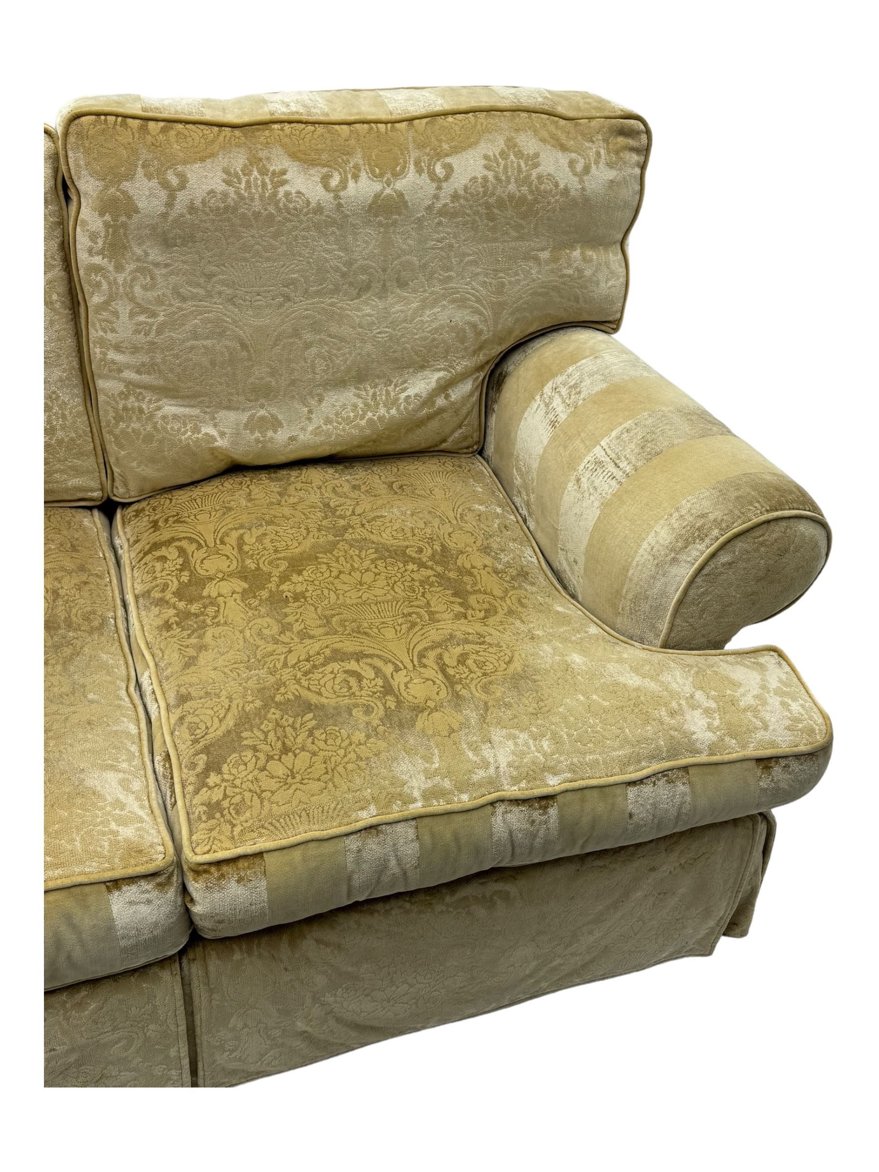 Contemporary two-seat sofa, upholstered in damask fabric with a pale gold floral pattern, rolled arms with covers, loose back and seat cushions, on matching skirted base with concealed castors