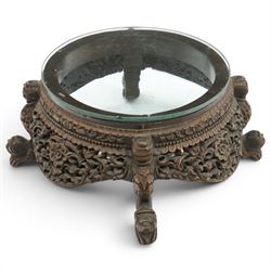 19th century Burmese carved hardwood jardinière stand, circular glazed top over pierced and carved floral frieze, on four zoomorphic supports carved with mythical beast masks and paw feet