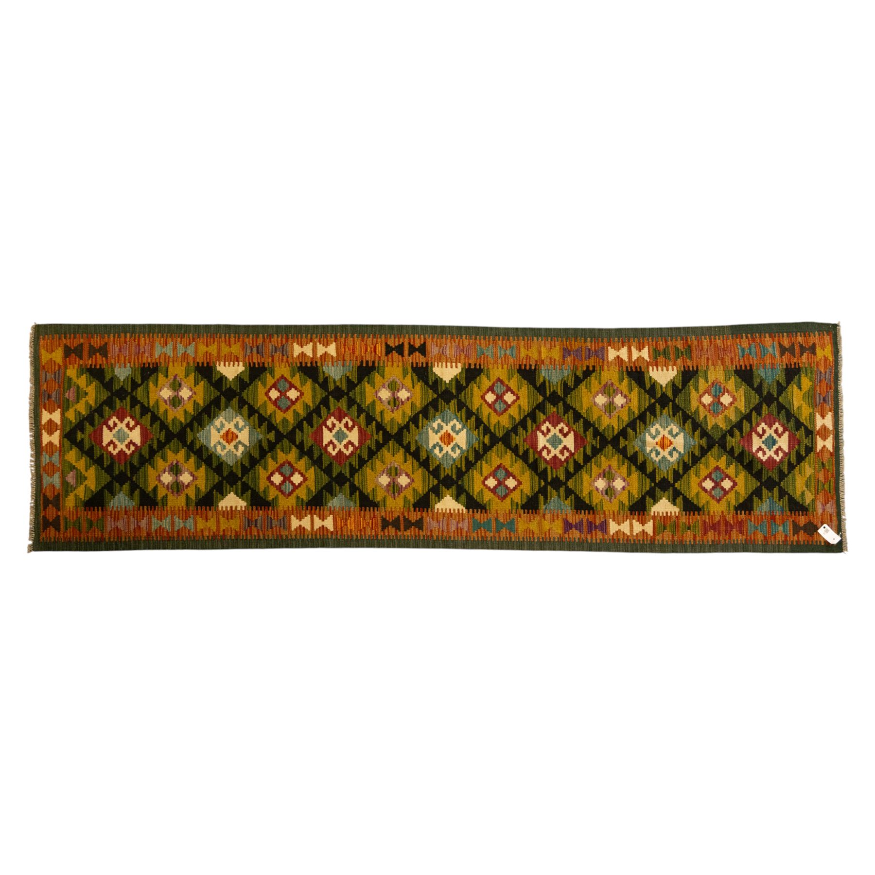 Chobi flatweave kilim runner with a repeating stepped diamond medallion design in live green, rust, teal, purple, and ivory, framed by chevron and geometric borders