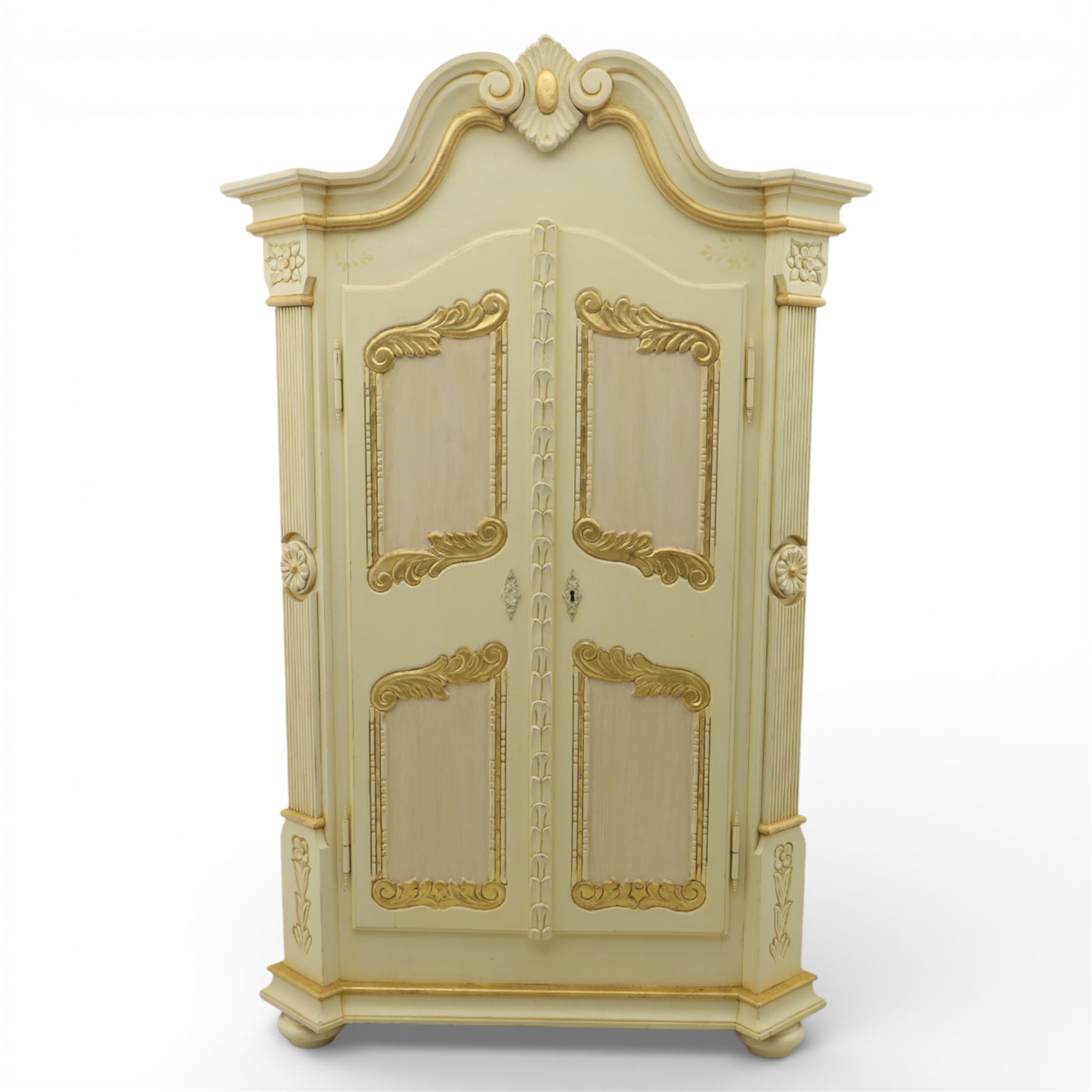 20th century French white and parcel gilt painted armoire, the shaped and scroll moulded cornice centred with a stylised foliate, the double doors with raised panel reserves applied with gilt foliate scrollwork, flanked by fluted pilasters with floral capitals, opening to a fitted interior with shelving and hanging space, raised on a moulded plinth on squat bun feet