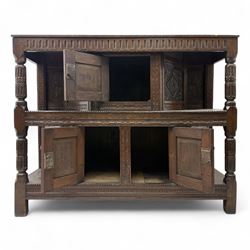 Early 20th-century  oak Jacobean two-tier revival court cupboard, rectangular top with carved notch and stylized foliate carved edge above a carved lozenge pattern frieze and a central cupboard with carved geometric designs and geometric carved panelled sides, above a carved panelled cupboard with two doors of similar geometric design, the whole flanked by two sets of stop-fluted baluster turned columns and supported on stile feet