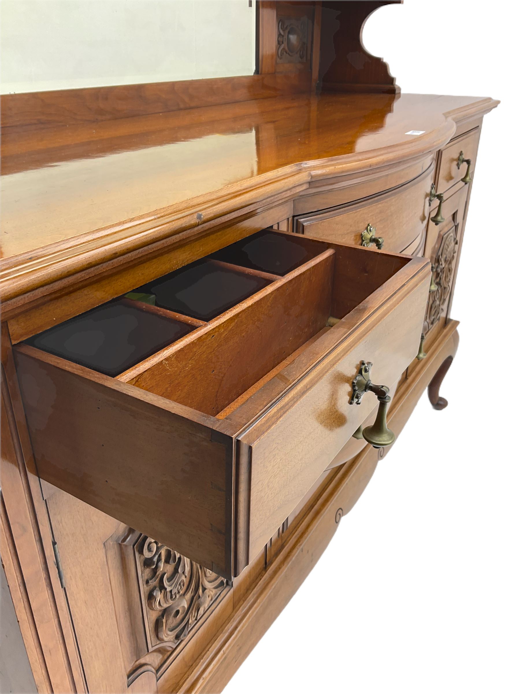 Late Victorian walnut mirror back sideboard or dresser, the raised back fitted with two curved and lead glazed cabinets, central arched bevelled mirror, the sideboard with break bowfront, fitted with six drawers and two cupboards, the cupboard doors panelled and carved with scrolls, shell and plant motifs, shaped apron with cabriole feet
