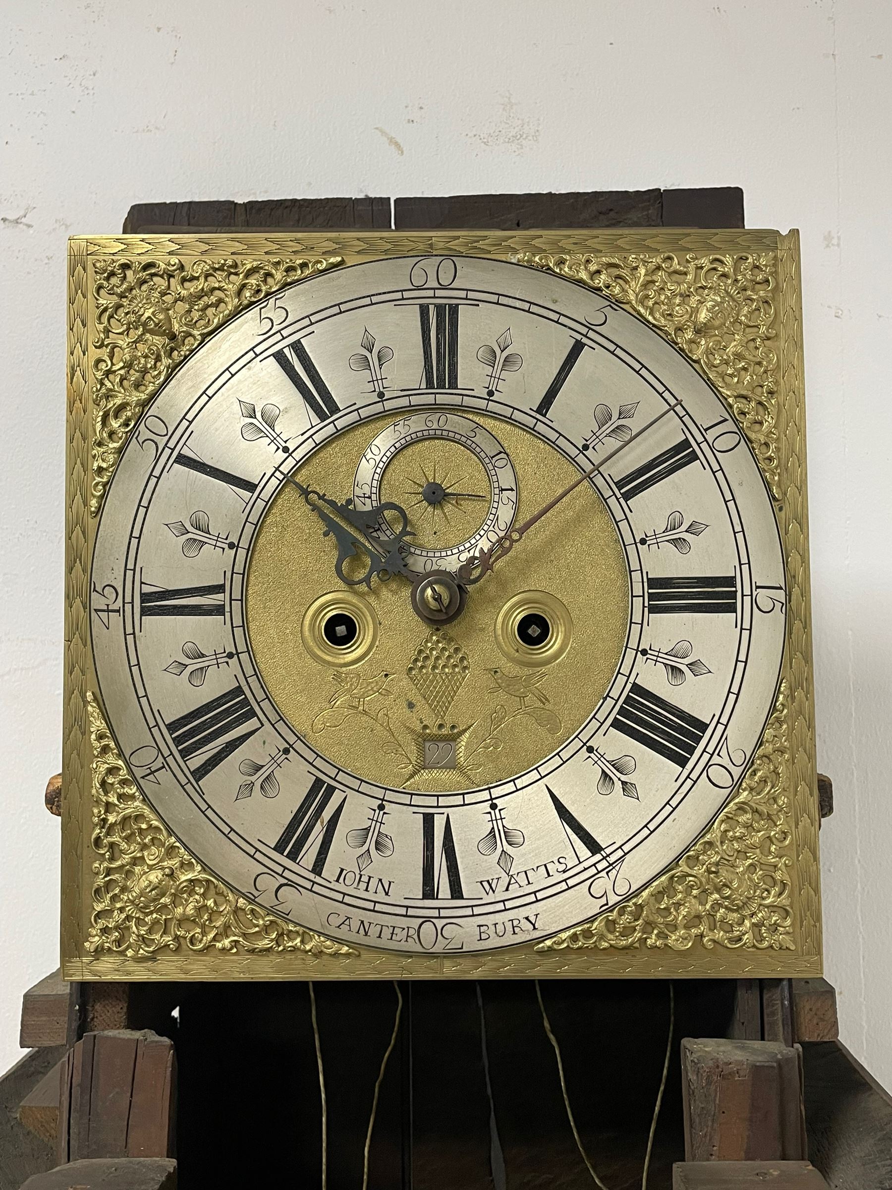 John Watts of Canterbury - early 18th century 8-day oak longcase clock, with a flat topped hood, broad cornice, dentil moulding and blind fret beneath, baluster turned pilasters with wooden capitals flanking the square hood door, trunk with recessed beaded edge and a long ogee topped door with crossbanding, plinth with applied skirting, square brass dial with matching steel hands, cast spandrels and a matted and engraved centre, date aperture, seconds ring and ring turned winding apertures, silvered chapter ring with Roman numerals, five minute Arabics, minute and quarter hour tracks, five pillar movement with a recoil anchor escapement and inside countwheel strike, sounding the hours on a bell. With weights and pendulum.
