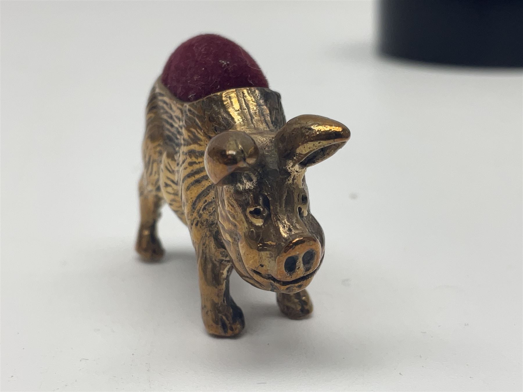 Three pin cushions, comprising gilt metal pig, silver plate shoe, circular pin cushion on threel feet, together with black pin holder with silver writing to the lid 