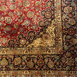 Central Persian Kashan hand-knotted carpet, crimson ground, with a large central ivory and dark navy floral medallion with pendants, surrounded by dense scrolling foliate and floral motifs incorporating rosettes, palmettes and vine work, enclosed by ivory spandrels and a dark navy border with repeating palmettes and meandering vines, flanked by floral guard stripes