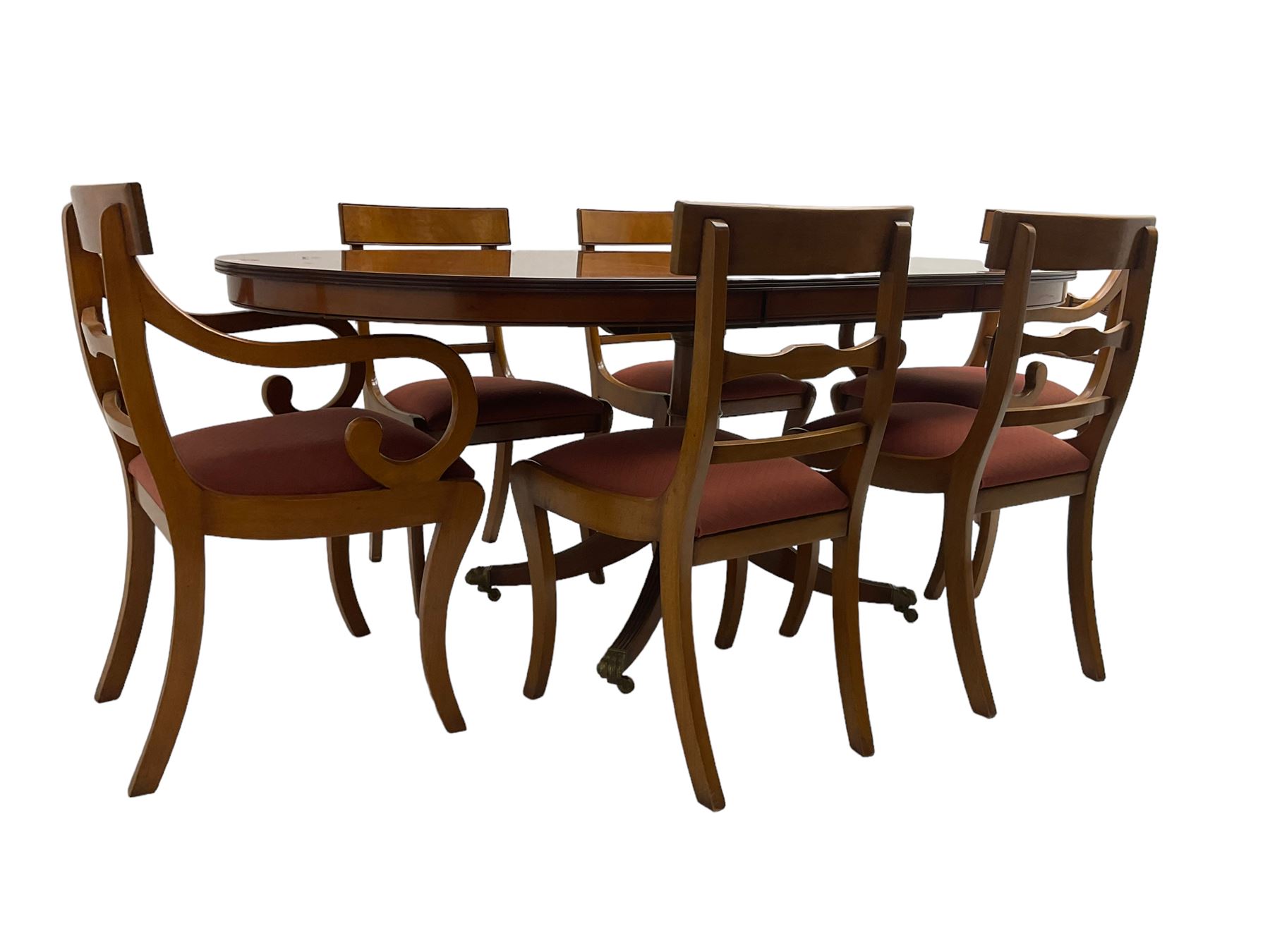 Regency design yew wood dining table, oval cross-banded top with reeded edge, raised on turned pedestal with reeded sabre supports terminating in brass hairy paw feet and castors (W138cm D100cm H75cm); and Rackstraw - set six (4+2) Regency design dining chairs with red drop-in seats (W50cm H86cm)