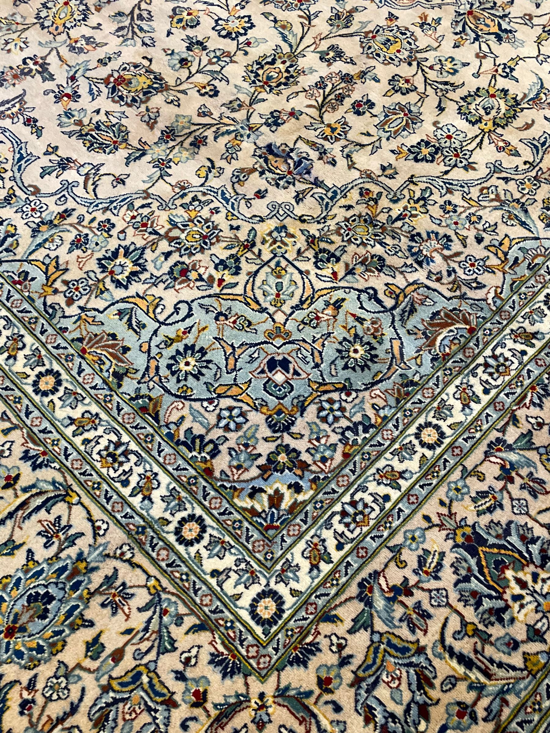 Central Persian Kashan pale khaki ground carpet, shaped central medallion enclosing small stylised motifs, the field decorated profusely with trailing foliate branches and plant motifs, guarded border with repeating floral design 