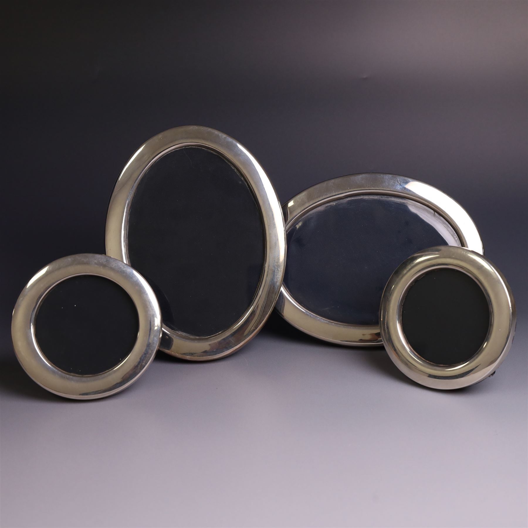 Four late 20th century silver mounted photograph frames, comprising two oval frames and pair of smaller circular frames, all hallmarked Laurence R Watson & Co, Sheffield 1983/4, largest H16.5cm
