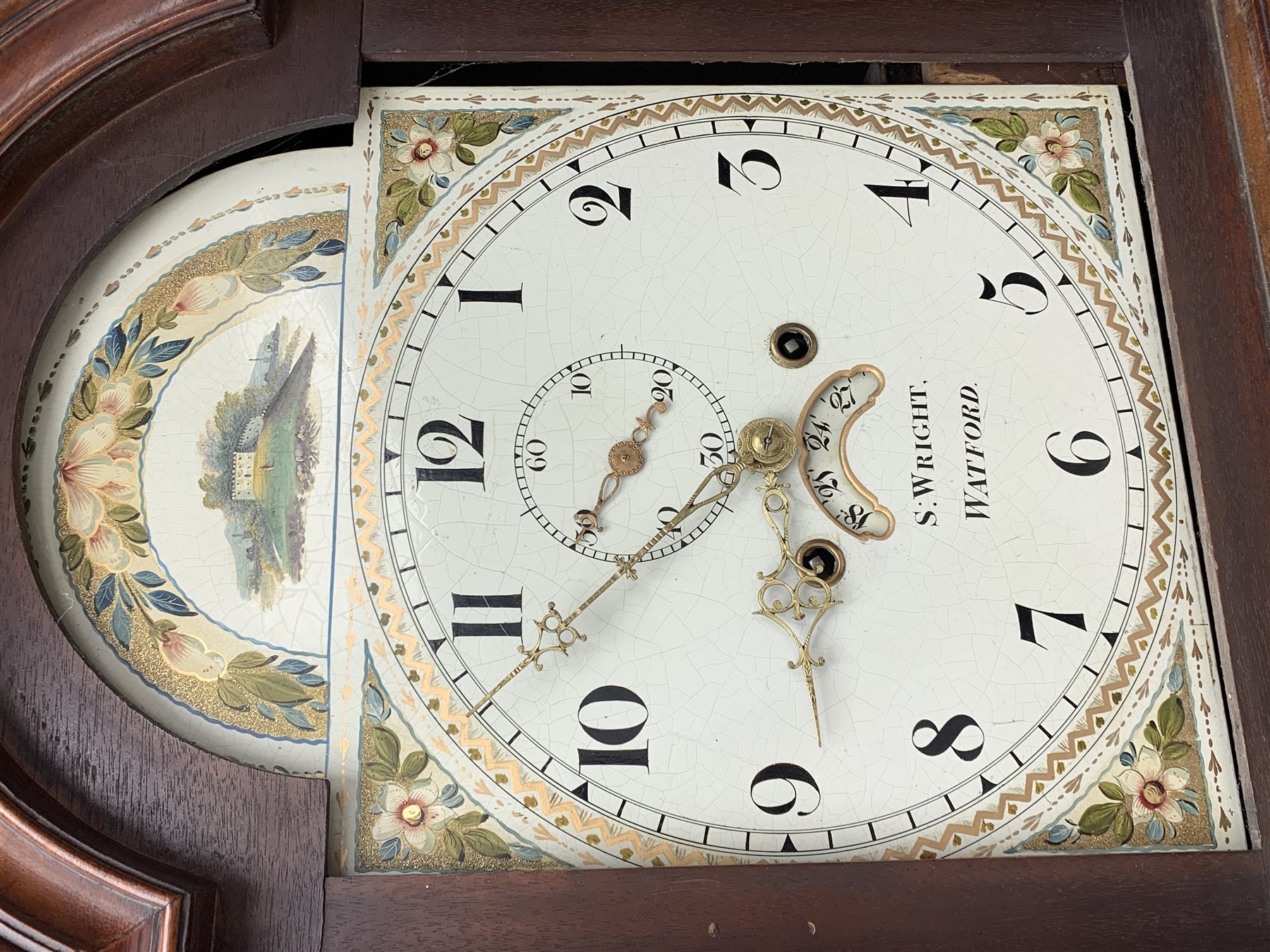 George III mahogany longcase clock, the hood with stepped moulded arch pediment above glazed door, fret work grille to each side, figured trunk door and base, enamel Arabic dial painted with country house scene and floral spandrels signed 'S. Wright, Watford', subsidiary seconds dial and date aperture, eight day movement striking the hours on bell, H212cm (two weights and pendulum)