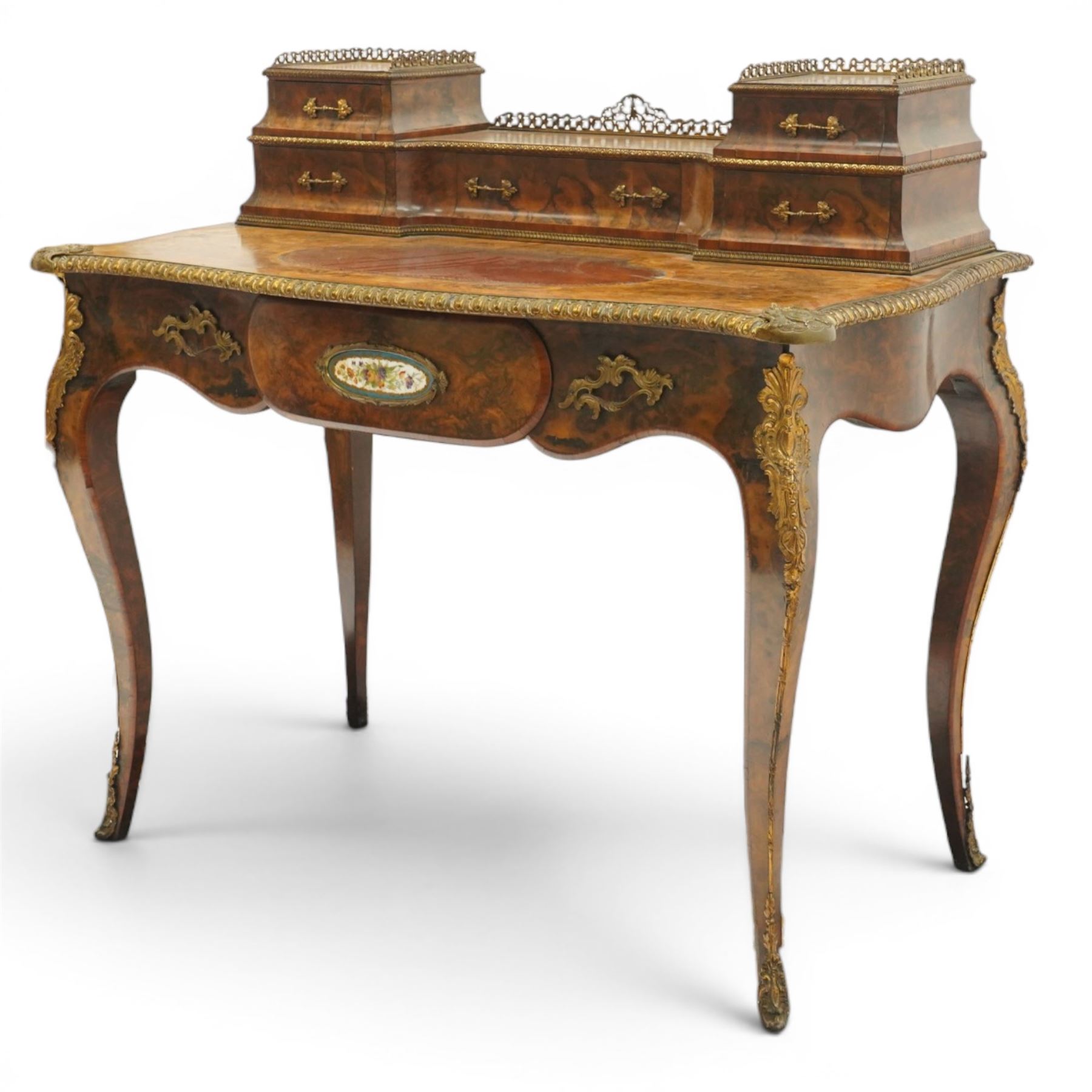 Victorian figured walnut and kingwood-banded ladies writing table, the raised superstructure with three-quarter pierced brass raised gallery back, fitted with five assorted drawers, the serpentine shaped top with oval inset leather surface, the bronze edge of egg and dart form with cartouche corners, fitted with central frieze drawer with inset Sevres-style floral ceramic plaque, raised on cabriole supports with gilt metal mounts