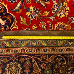 Central Persian Kashan hand-knotted carpet, central field in a ruby red ground with an indigo medallion with pendant motifs, enclosing scrolling arabesques, palmettes, and floral sprays in shades of indigo, turquoise, ivory, and gold, framed by indigo spandrels and a broad floral border between multiple guard stripes 