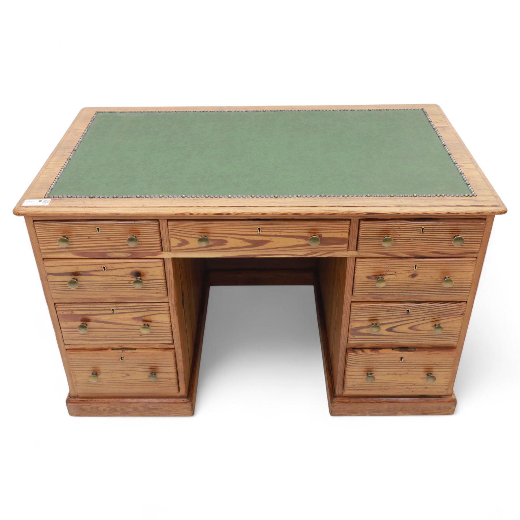 Contemporary stripped and waxed pine pedestal kneehole desk, rectangular top inset with green leather writing surface with brass studded edge, fitted with nine drawers with brass knob handles, above a plinth base on recessed castors