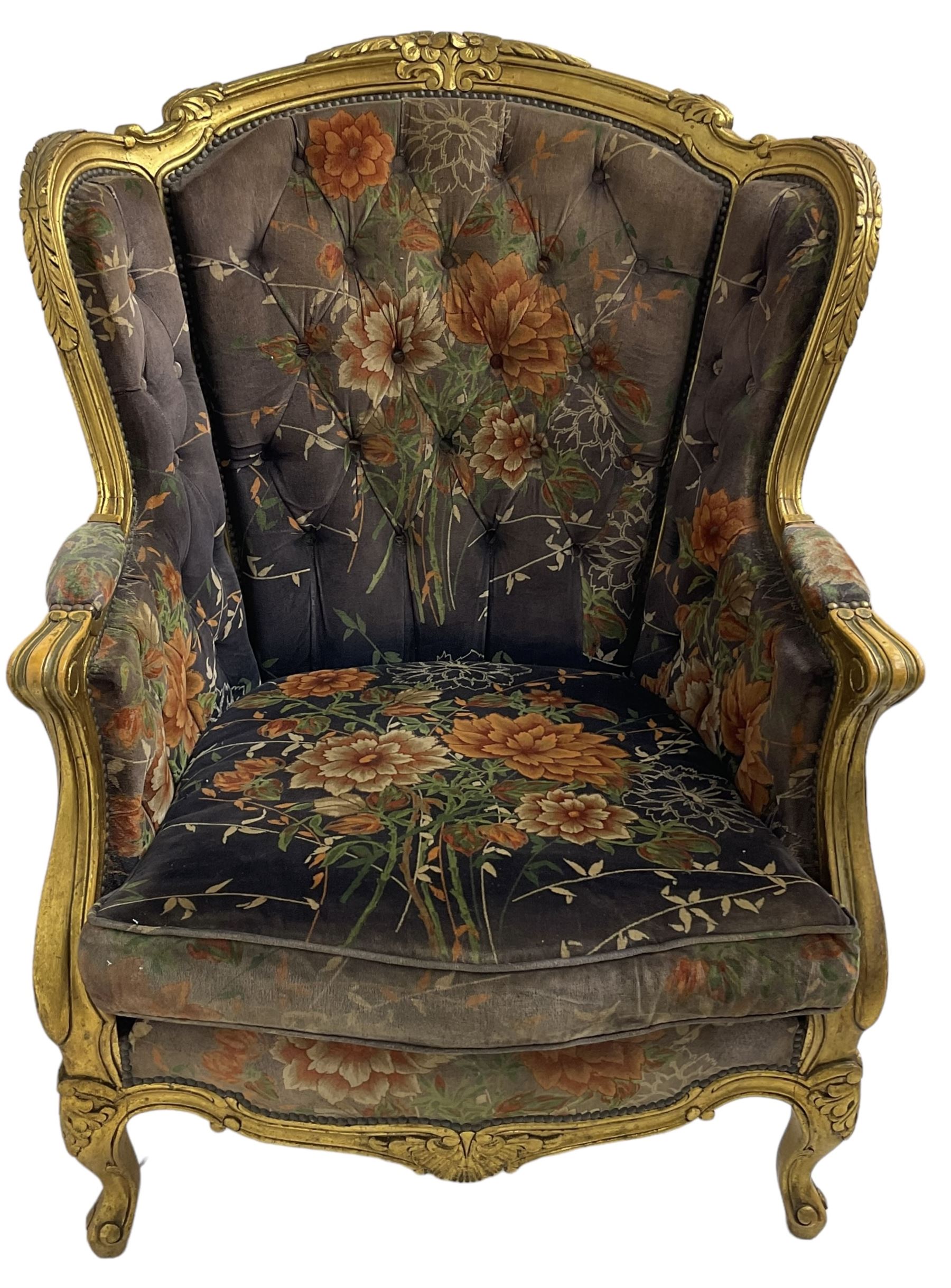 Pair of Louis XVI design gilt framed wingback armchairs, cresting rail carved and moulded with foliate decoration and C-scrolls, upholstered in buttoned floral patterned mauve velvet with loose seat cushion, scallop carved apron over cabriole supports