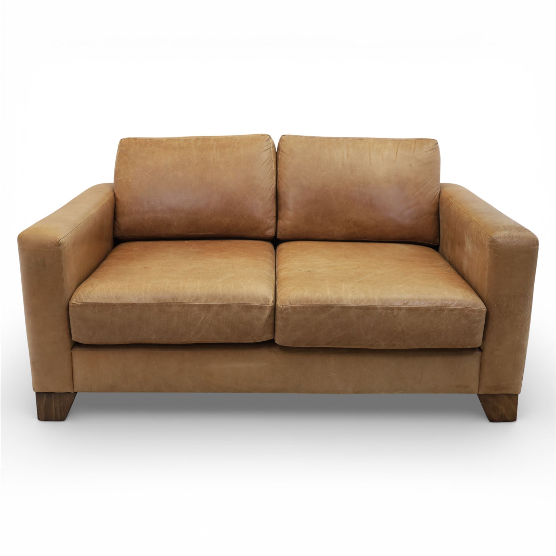 Modern two seat sofa in tanned leather, loose seat and base cushions, block arm rests above dark stained block supports 