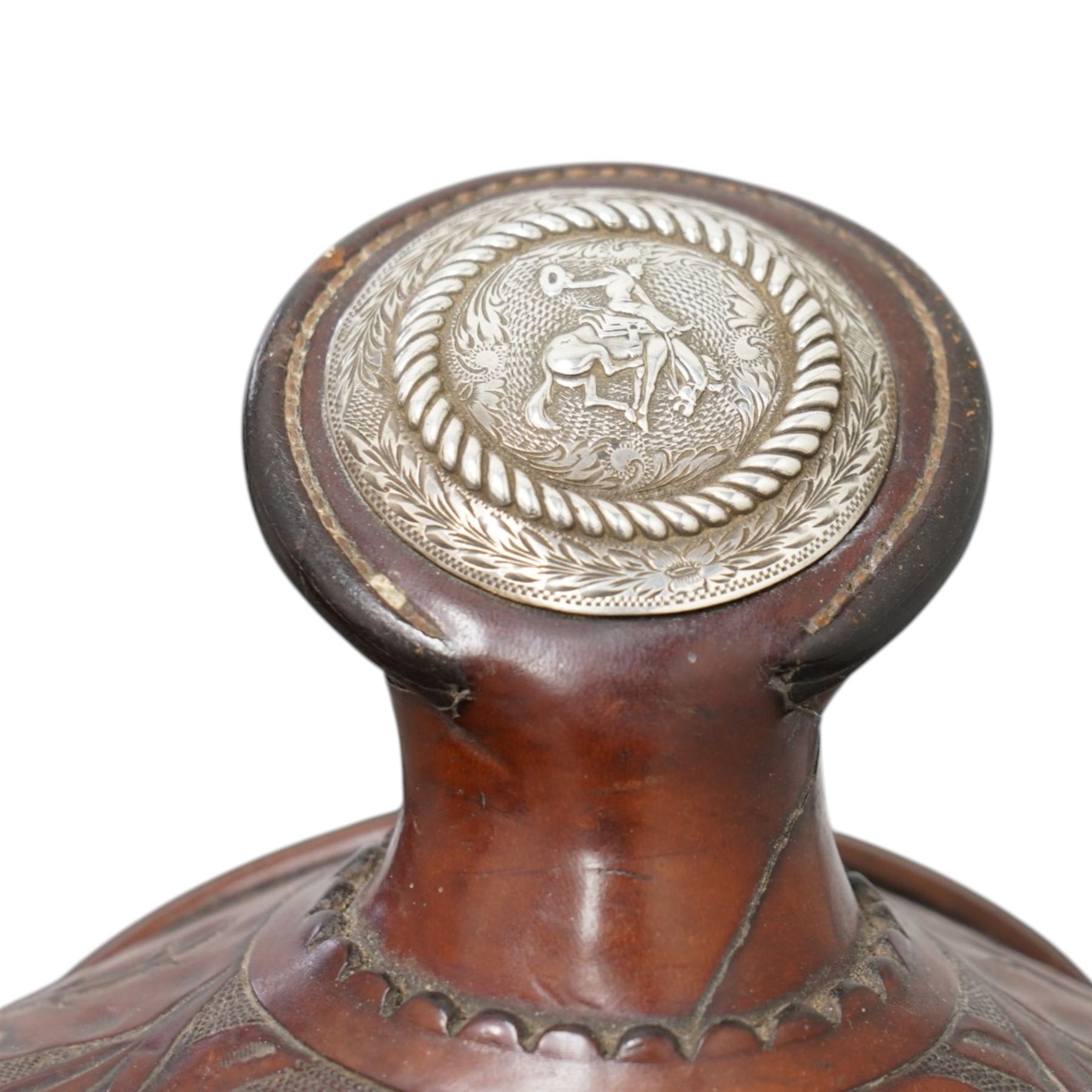 Keyston Bros (San Francisco) - 1930s/1940s 18’ American leather and silver mounted Western Parade saddle, the mahogany-tone leather body heavily hand-carved in a deep California Poppy floral pattern, surmounted by a ‘Bear Trap’ pommel fitted with an oval horn cap featuring a silver medallion of a cowboy on a bucking horse, further embellished with engraved sterling silver mountings, including large domed conchos, full-dress skirt corner plates, and a continuous cantle trim band, together with the associated girth, stirrups and leathers