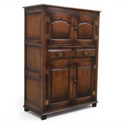  Late 20th century oak four door cupboard in the manner of Titchmarsh and Goodwin, rectangular plank top above two pairs of fielded panel doors with shaped raised panels, central arrangement of a brushing slide above two short drawers with brass swan neck handles and pierced backplates, enclosed by further pair of panelled cupboard doors, fitted with brass butt hinges and turned wooden knobs, raised on plinth base