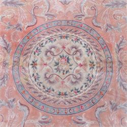 Large late 20th century Aubusson style wool carpet, peach and pastel toned field with central floral medallion enclosing scrolling acanthus and and foliate sprays, surrounding field decorated with further stylized foliage and and floral ornament, within shaped reserves and indigo corner spandrels, enclosed by narrow guard border, cotton fringe ends