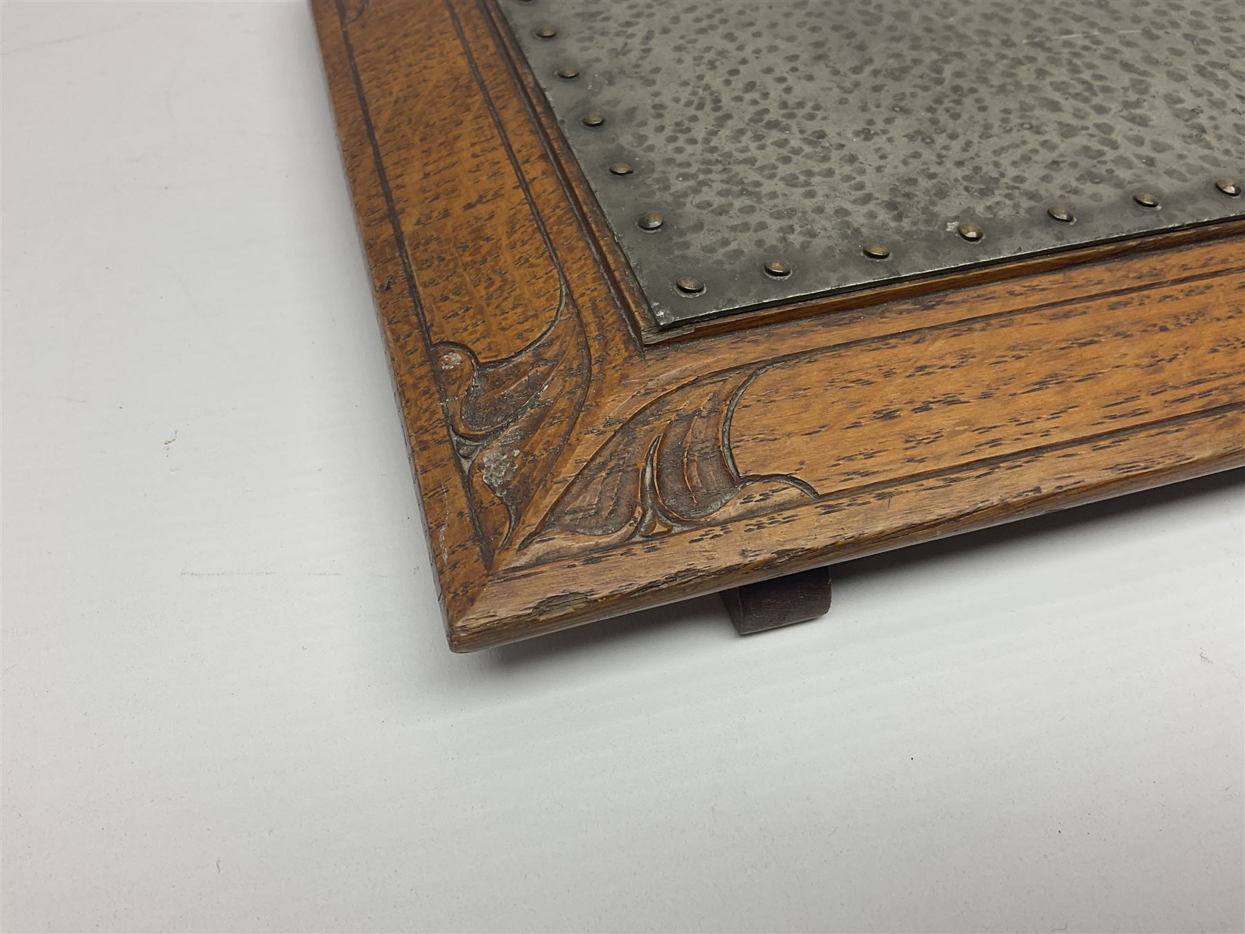 Arts and Crafts oak stand by Arthur Simpson of Kendal, of rectangular form with central hammered pewter panel, surrounded by a border with carved foliate corners, upon two bar supports, bearing label detailed 