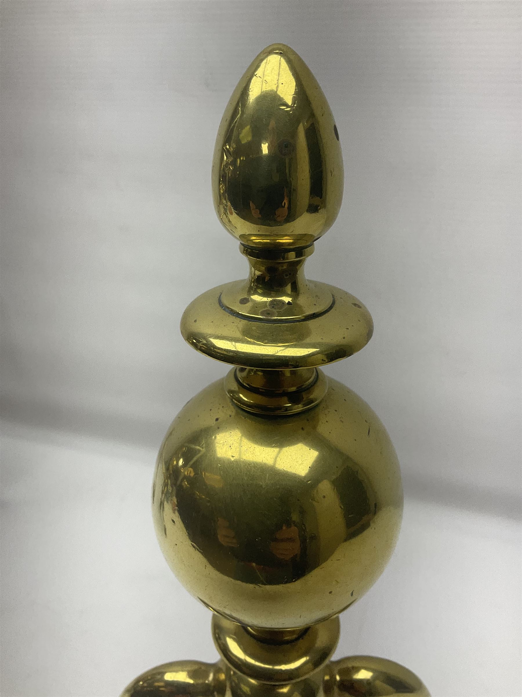 Pair of early 20th century brass fire dogs, each with sphere and urn finial, upon a scrolling base, H38cm
