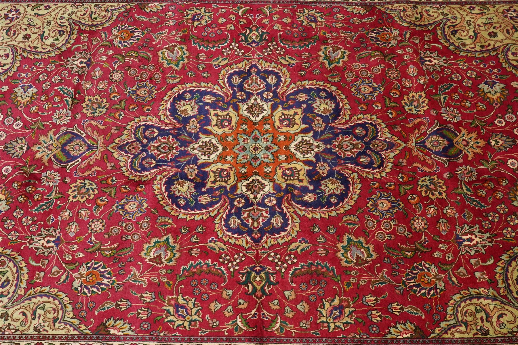 North East Persian Meshad hand-knotted carpet, crimson field with central lobed medallion in tones of indigo, ivory and soft blue, with an all-over arrangement of scrolling vinery, palmettes, and floral  sprays, conforming spandrels, main border of stylized floral vinery framed by multiple guard borders, with cotton fringe ends
