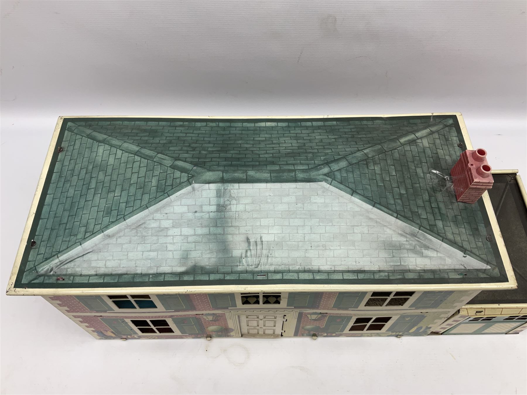Mid-20th century Mettoy tin-plate double-fronted two-storey doll's house, the front elevation with five unglazed windows flanked by green shutters, central opening door, open back giving access to five rooms together with an attached garage, 60cm wide