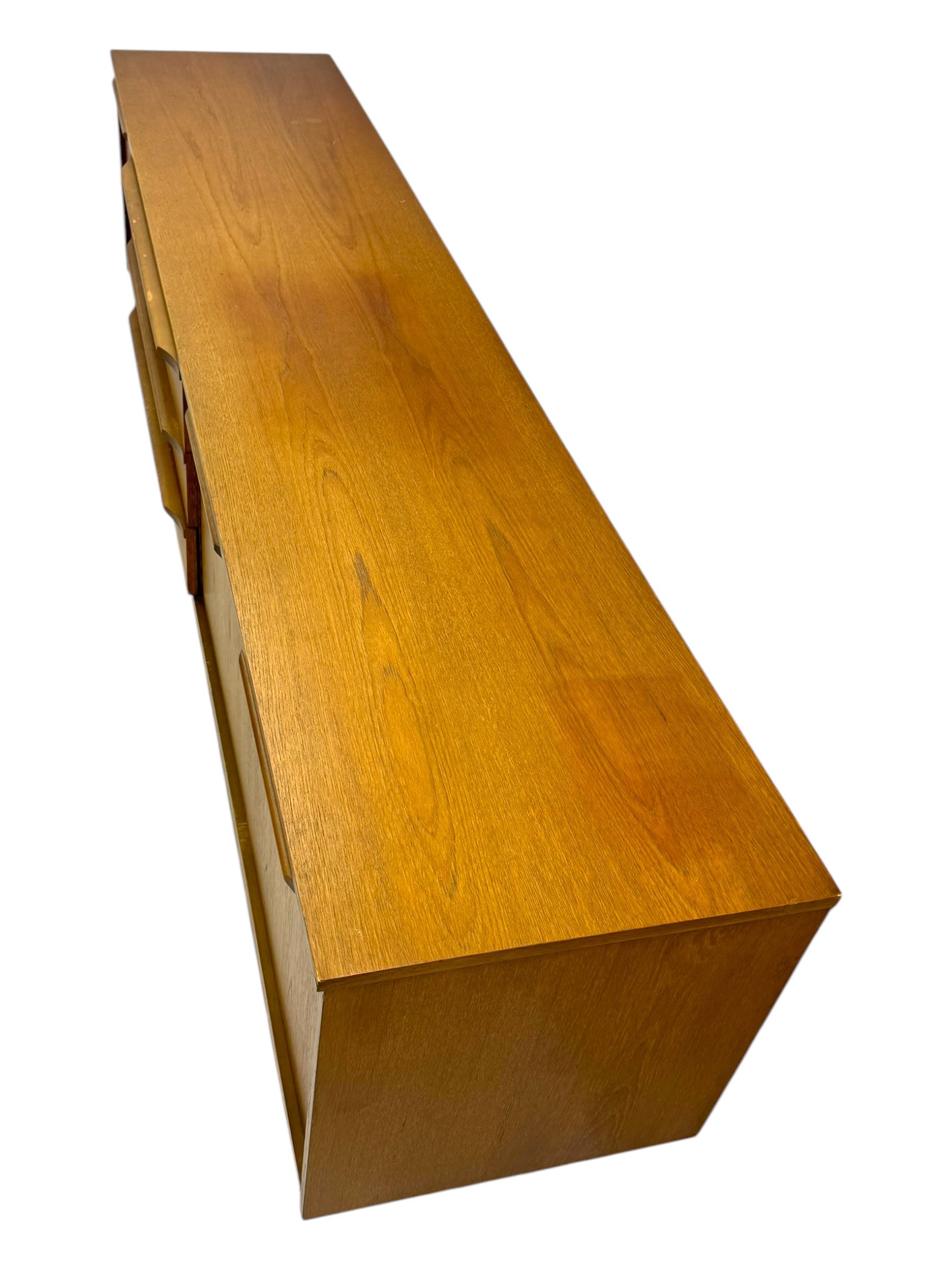 Mid-20th century teak sideboard, fitted with a fall-front cupboard, three drawers including a green baize-lined cutlery drawer, and a double cupboard, with integrated handles, on sleigh supports