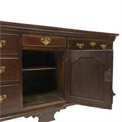 19th century Georgian oak long dresser base, rectangular plank top above a central frieze drawer over a fielded panel cupboard, flanked by three banks with quarter cantered pilasters, brass swan neck handles and escutcheons, raised on shaped bracket feet