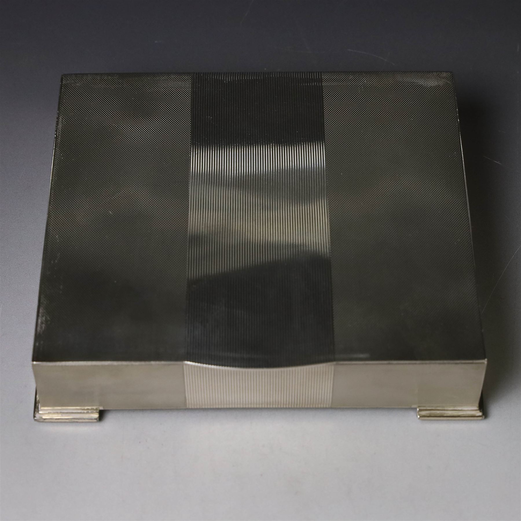 1960s silver mounted cigarette box, of rectangular form with engine turned decoration, upon four bracket feet, with presentation engraving to interior lid reading  'British Aircraft Corporation (Operating) Limited Commemorating the Queen's Award to Industry 1967, hallmarked James Geraghty, Birmingham 1965, with retailers mark for Asprey, W16.5cm, H4.5cm, in Garrard & Co Jewellers box