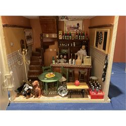 Seagull Pub - scratch-built wooden doll's house as a two-storey gable fronted public house painted in white green and maroon; the hinged front with ground floor veranda and window over opening to reveal two fully furnished rooms with dog-leg staircase and well stocked bar with bar-tender L31cm H62cm D37cm; together with Corner Shop and Dollies Pantry; a similarly painted scratch-built wooden two-storey flat-roofed doll's house as a well stocked ground floor grocery shop with stairs up to two further fully furnished rooms and more stairs giving access to a roof terrace L46cm H57cm D33cm (2)