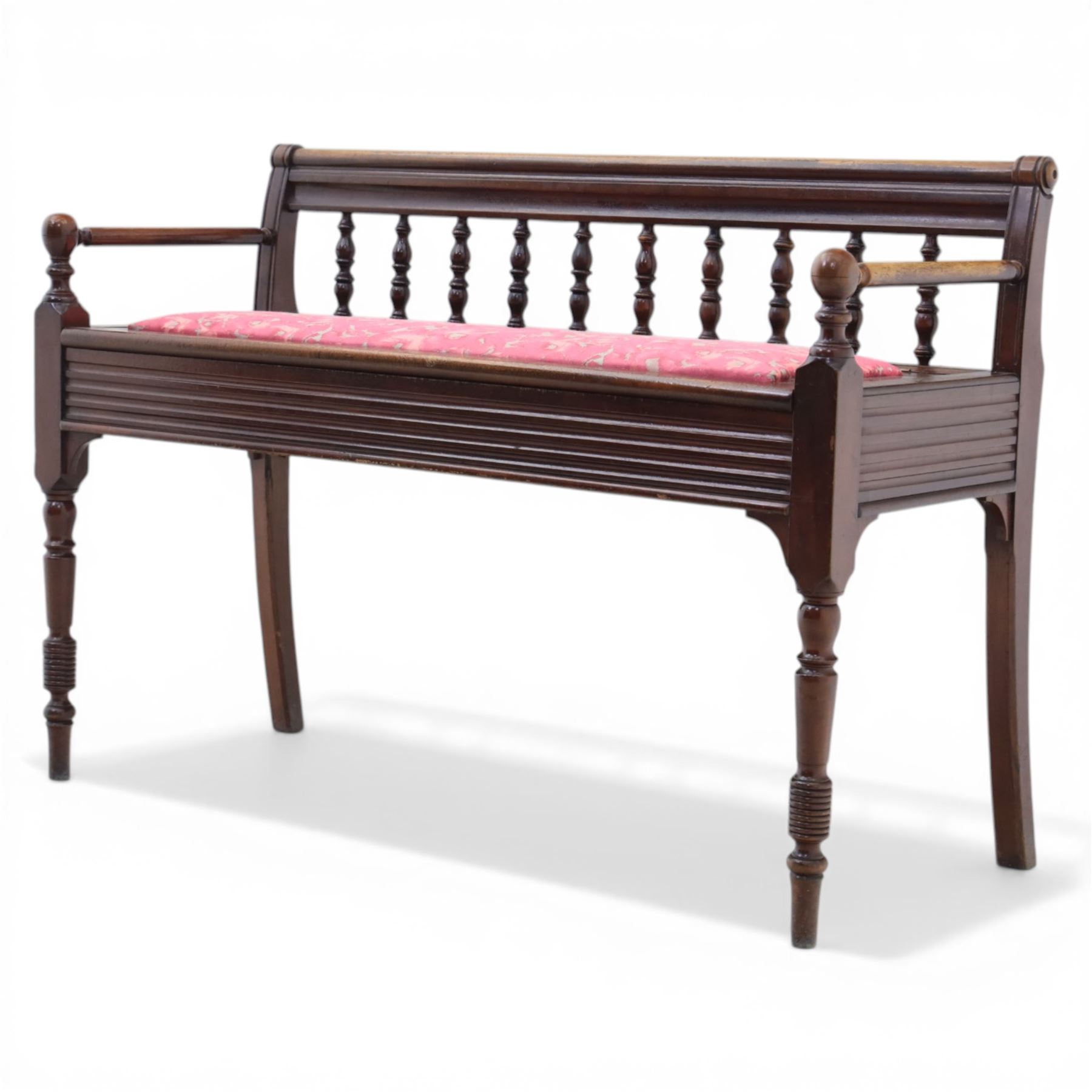 Early 20th century mahogany hall bench, spindle turned back with shaped top rail and open arms terminating in ball finials, upholstered seat within a fluted frieze, raised on turned tapering supports