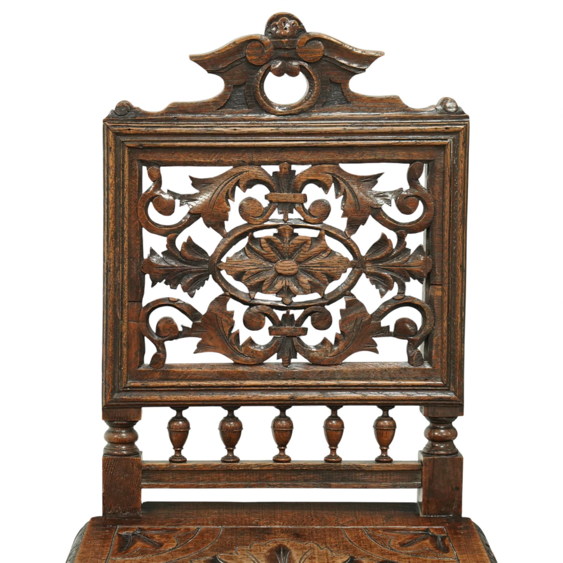 18th century carved oak hall chair, the rectangular pierced back carved with scrolling foliate ornament and central rosette beneath a shaped cresting, the boarded seat carved with stylised foliage, raised on turned legs united by stretchers