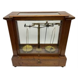 Set of brass balance scales in glazed mahogany case, with frieze drawer opening to reveal boxed weights, raised on four brass screw feet, H45cm W45.5cm D22.5cm