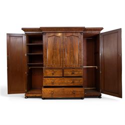 Early 19th century figured mahogany combination wardrobe, the breakfront architectural cornice over central press cupboard enclosing linen slides, flanked by full-height hanging cupboards with arched inset panels, lower arrangement of two short and two long drawers with turned knob handles, applied acanthus carved detail, raised on bun feet