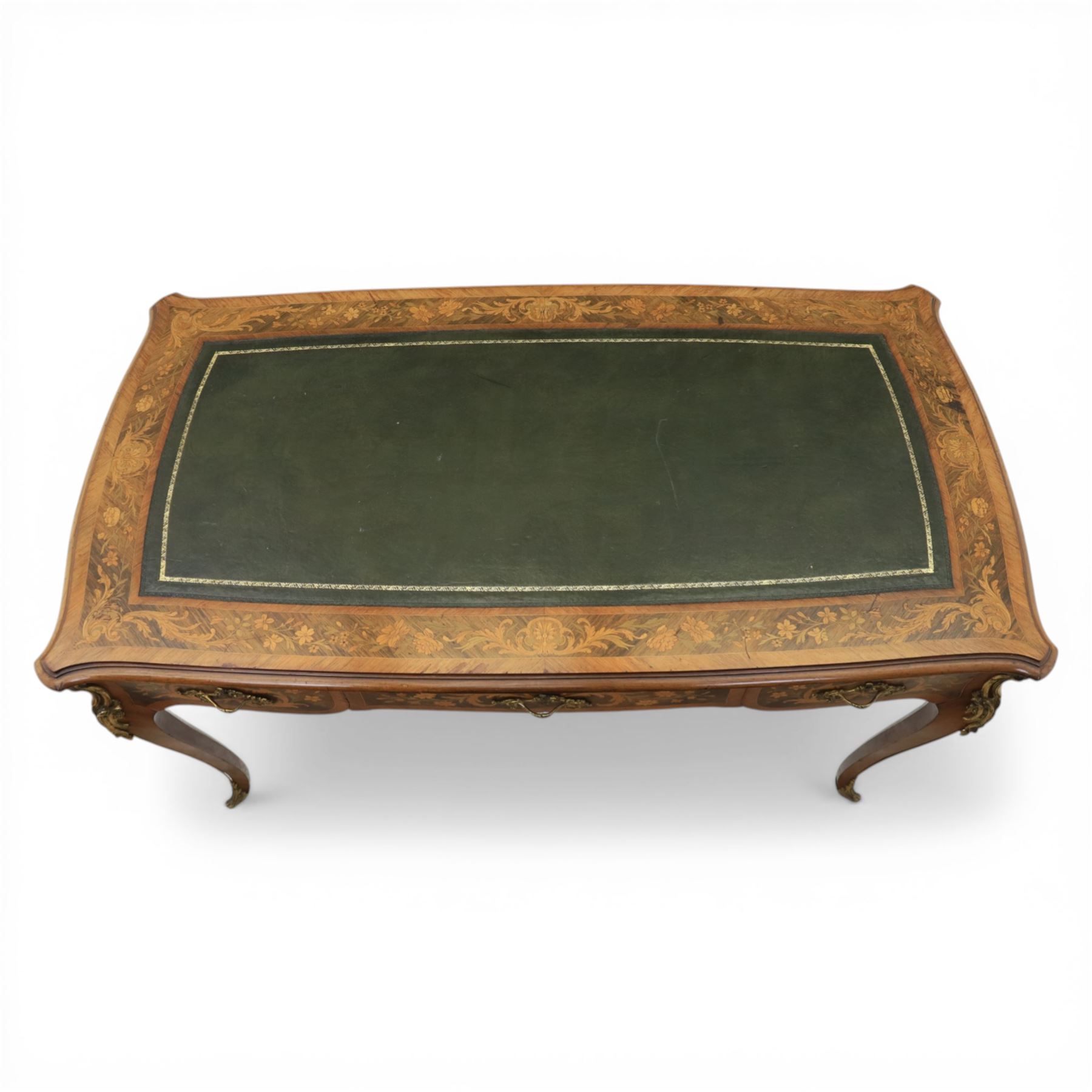 Late 19th century French kingwood and marquetry bureau plat, the serpentine rectangular top with green leather inset writing surface within crossbanded and foliate marquetry border, above a shaped frieze fitted with three drawers with floral marquetry panels and gilt metal handles, upon cabriole supports with applied gilt metal mounts and sabots