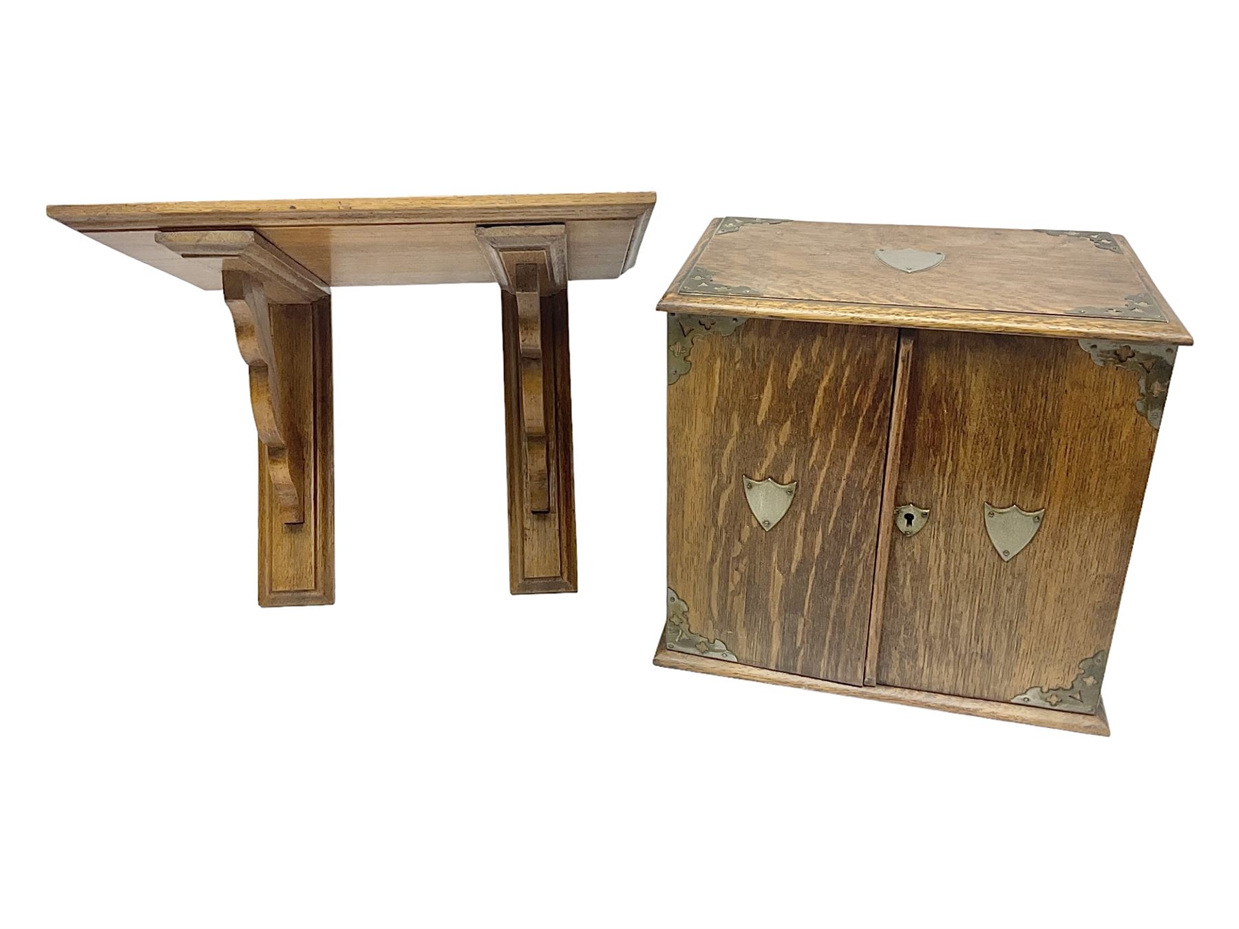 Early 20th century oak smokers cabinet, with brass shield shaped mounts, opening to reveal a compartmentalised interior with three drawers, pipe rack and tobacco jar, together with a small wooden shelf, smokers cabinet H28.5cm