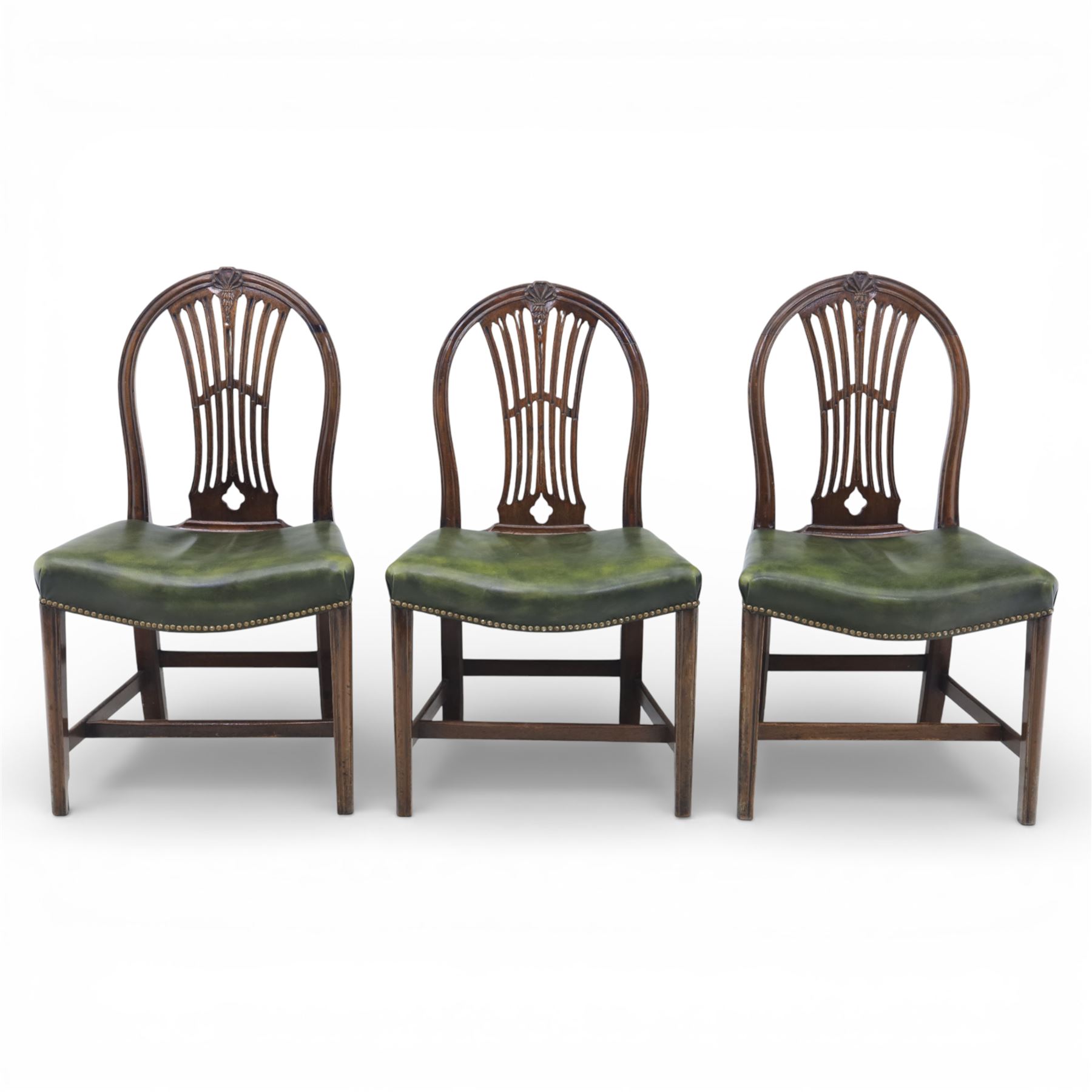 George III style set of six mahogany dining chairs, the arched backs with pierced and carved vase splats beneath carved husk and patera detail, drop-in upholstered seats covered in green leather with brass studded edging, raised on square section legs united by plain stretchers